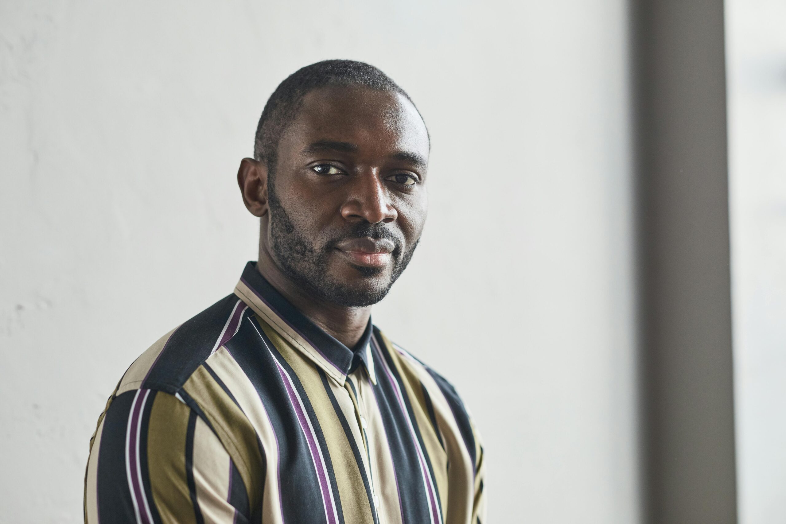 Close-up portrait of a confident man with a beard in a striped shirt, indoors.